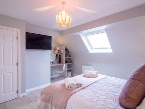 A bedroom with a bed, a desk, a chair, a radiator, and a skylight.