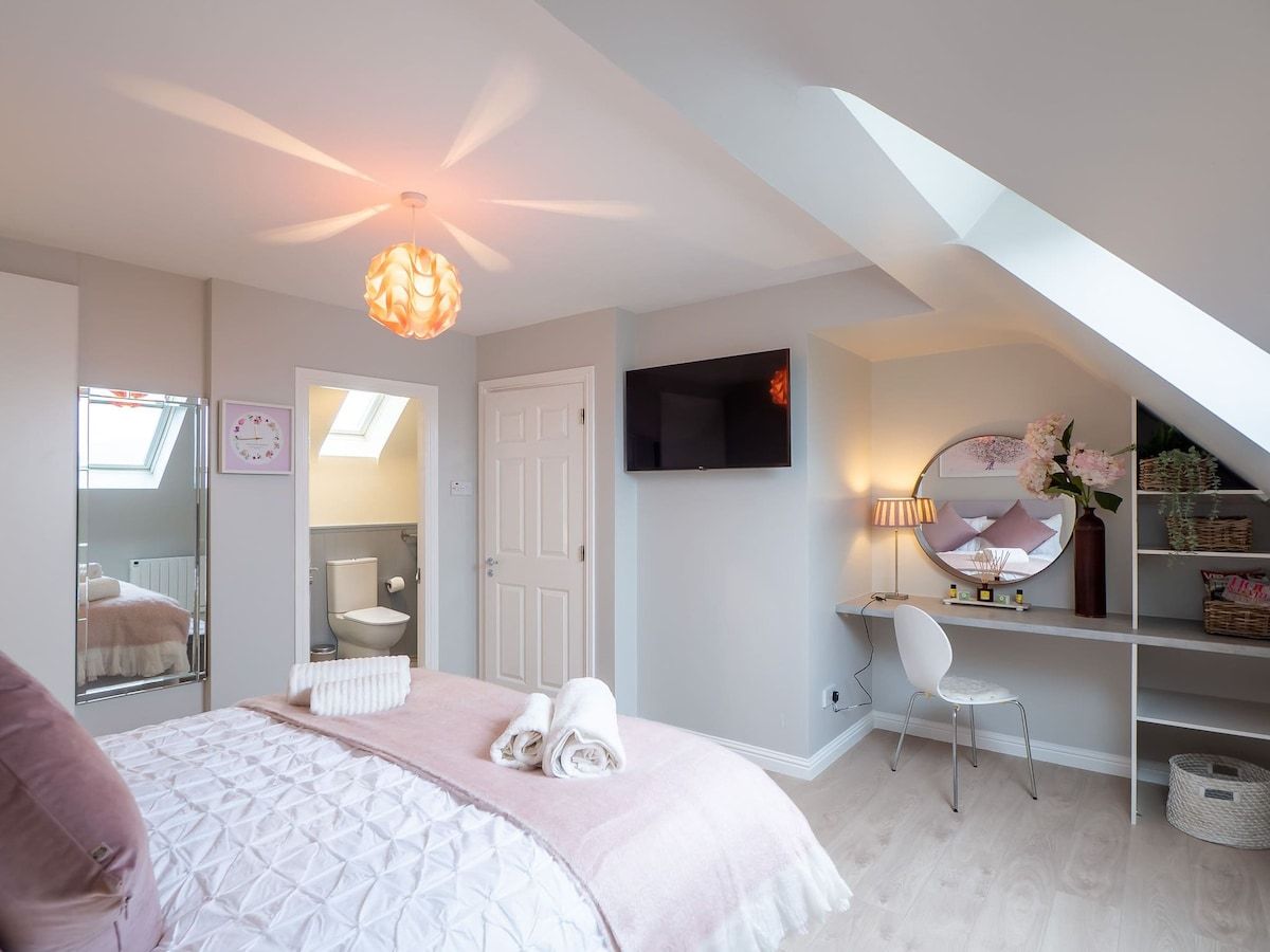 Een slaapkamer met een bed, een bureau, een stoel, een televisie en een dakvenster.