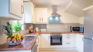 Eine moderne Küche mit weißen Schränken, einer Holzarbeitsplatte, einem eingebauten Backofen, einer Mikrowelle und einer Obstschale.