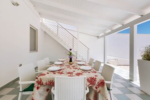 En spiseplads med et bord dækket til seks personer, hvide stole og en trappe til en etage ovenover.