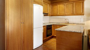 Une cuisine avec des meubles en bois, un réfrigérateur blanc, un four et un plan de travail en granit.