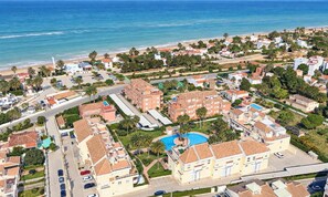 A coastal residential area with multiple buildings, a central swimming pool, and a beach in the background.