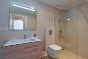 A modern bathroom with a white sink, wooden vanity, a toilet, and a glass-enclosed shower area.