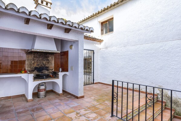 A patio with a grill, a tiled backsplash, and a metal barrel.