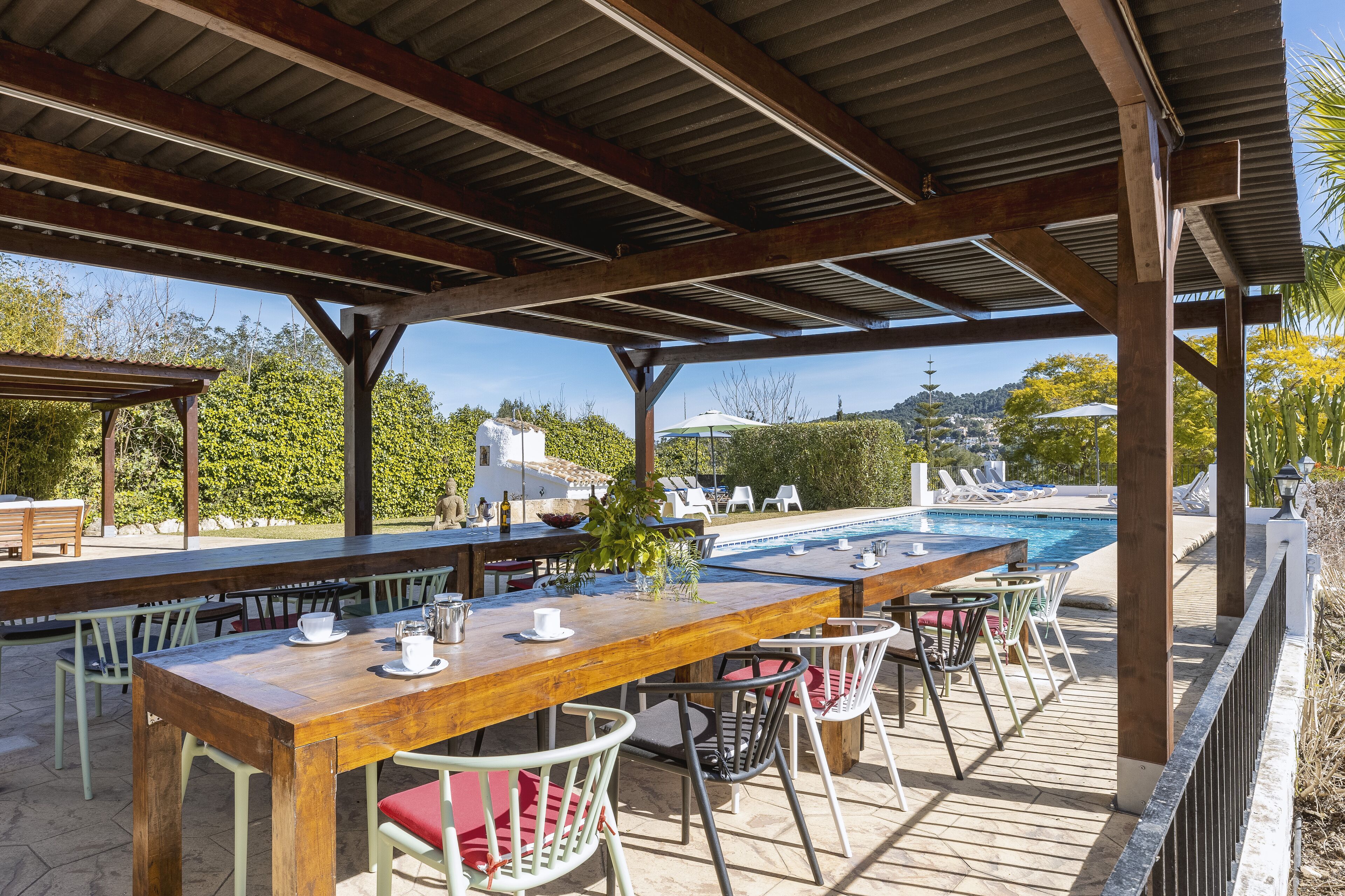 An outdoor patio with a wooden table and chairs, a pool, and a view of the surrounding landscape.