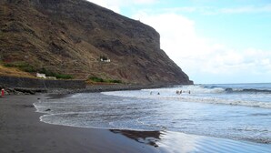 Una playa con un acantilado rocoso, olas y algunas personas en el agua.
