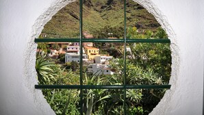 Vista a través de una ventana circular con diseño de cuadrícula, que muestra una ladera con edificios y abundante vegetación.
