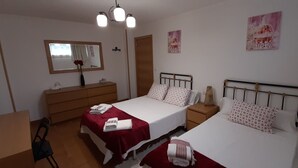 Quarto com duas camas, uma cômoda de madeira, um espelho e uma escrivaninha.