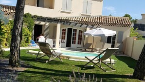 A house with a swimming pool, two lounge chairs, and a covered patio area.