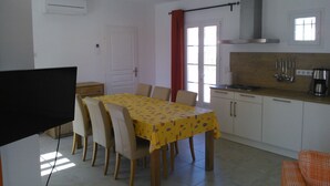 A dining area with a table set for six, a kitchen with a stove and sink, and a TV in the corner.