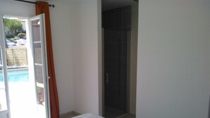 A bedroom with a bed, a shower area, and a view of a swimming pool.