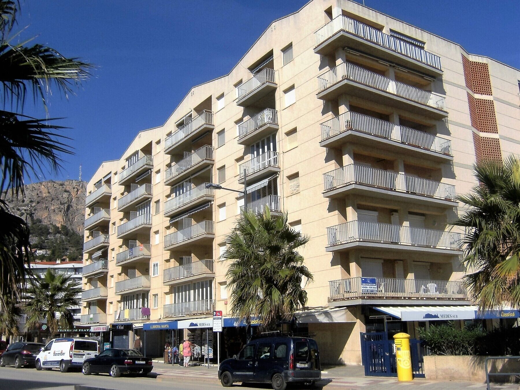 A multi-story building with balconies, a storefront, and parked cars.