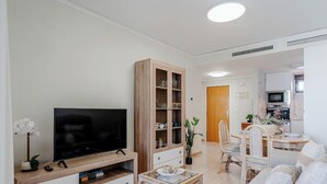 A modern living room with a flat-screen TV, wooden cabinet, dining area with chairs, and a kitchen in the background. - Nautilus 39B - Grupo Turis - Calpe, Costa Blanca (Calpe)