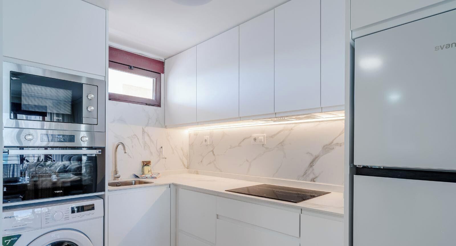 Een moderne keuken met inbouwapparatuur, een wasmachine en een marmeren achterwand.