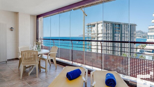 A balcony with a view of the sea and buildings, a table with chairs, and a massage table with towels. - Nautilus 39B - Grupo Turis - Calpe, Costa Blanca (Calpe)