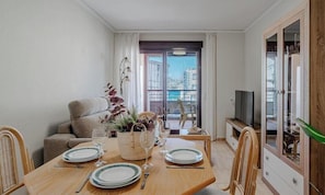 A dining area with a table set for two, a sofa, and a TV stand.