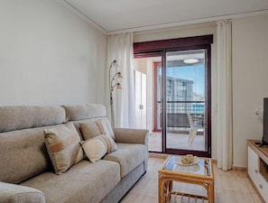 A living room with a sofa, a glass coffee table, a TV, and a sliding glass door leading to a balcony.