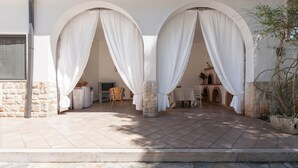 A covered outdoor seating area with stone pillars, a television, and a table with chairs. - Villa Ricci by Perle di Puglia (Ceglie Messapica)