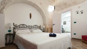 A bedroom with a large bed, a stone arch, a white wall, and a door leading to another room. - Villa Ricci by Perle di Puglia (Ceglie Messapica)