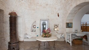 A stone-walled room with a round table, a wooden stool, and a large wooden column. - Villa Ricci by Perle di Puglia (Ceglie Messapica)