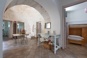 Una habitación rústica con un arco de piedra, una cama de madera, una mesita con una cesta y un banco.