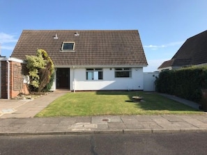 A single-story house with a tiled roof, a small front yard, and a paved driveway.