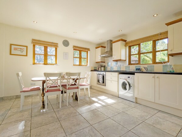 A kitchen with a dining table, chairs, a washing machine, and a clock on the wall.