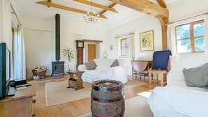 Quarto rústico com vigas de madeira aparentes, um sofá branco, um barril de madeira, um relógio e uma janela com cortinas.