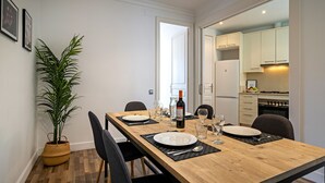 Un comedor con una mesa de madera dispuesta para dos personas, una planta en maceta y vistas a la cocina.