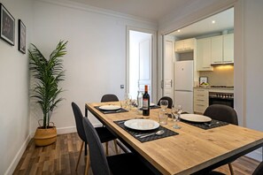 A dining area with a wooden table set for four, chairs, a potted plant, and a bottle of wine.