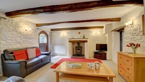 A cozy living room with a stone wall, a fireplace, a leather sofa, a wooden coffee table, and a television. - 3 Bed in Barnstaple (oc-n1991) (Bratton Fleming)