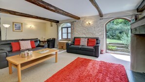 A living room with a fireplace, two sofas, a coffee table, and a large window. - 3 Bed in Barnstaple (oc-n1991) (Bratton Fleming)