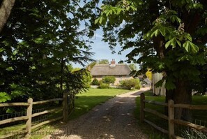 A rural pathway leading to a thatched-roof house surrounded by lush greenery. - The Dairy , Birdham  -  a barn conversion that sleeps 4 guests  in 2 bedrooms (Chichester)
