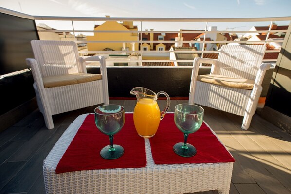A rooftop terrace with wicker chairs, a red tablecloth, and a pitcher of orange juice.