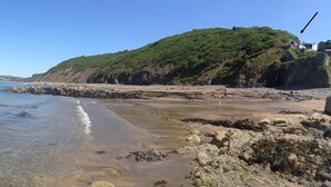 A rocky beach with clear water, a green hill with buildings, and a clear sky. - 2 Bed in Bideford (oc-willi) (Buck's Mills)