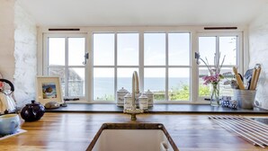 A kitchen with a large window overlooking the sea, a sink, and various kitchen utensils. - 2 Bed in Bideford (oc-willi) (Buck's Mills)