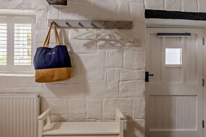 A room with a white brick wall, a coat rack with a blue and tan bag, a white bench, and a door with a window.