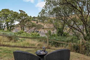 A wicker table with a book and a cup, overlooking a natural landscape with trees and rocky hills.