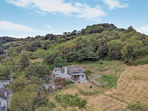 A hillside house with a thatched roof, surrounded by dense greenery and a clear sky.