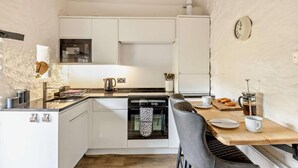 A compact kitchen with white cabinets, a microwave, a kettle, and a coffee maker.