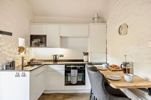 A compact kitchen with white cabinets, a microwave, a kettle, and a coffee maker.