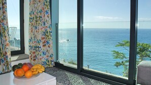 A room with a large window overlooking the sea, a fruit bowl on a white table, and a chair near the window. - Beachfront cottage in Calheta | Cottage do Mar (Arco da Calheta)