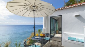 A table with a white umbrella, a glass of orange juice, and a fruit bowl on a balcony overlooking the sea. - Beachfront cottage in Calheta | Cottage do Mar (Arco da Calheta)