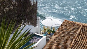 A rooftop pool with a view of the ocean, a white umbrella, and a tiled roof. - Beachfront cottage in Calheta | Cottage do Mar (Arco da Calheta)