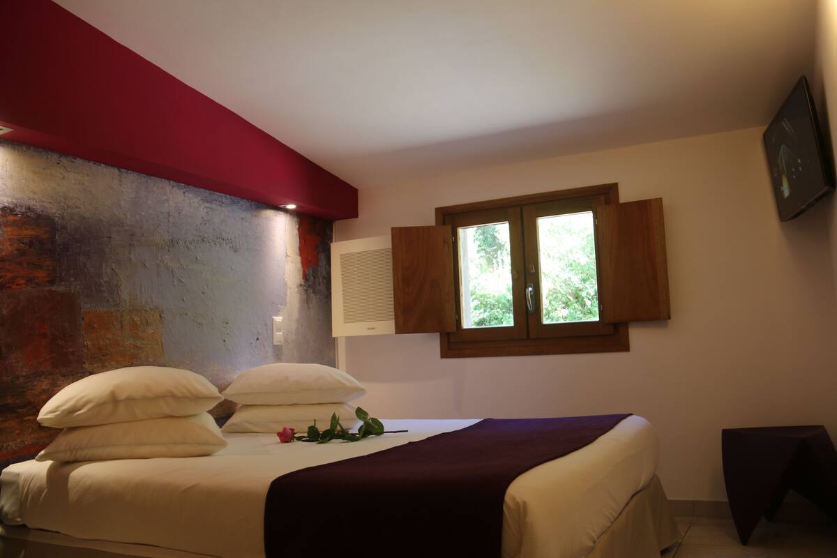 Un dormitorio con cama, almohadas, una ventana y un muro con una viga roja.