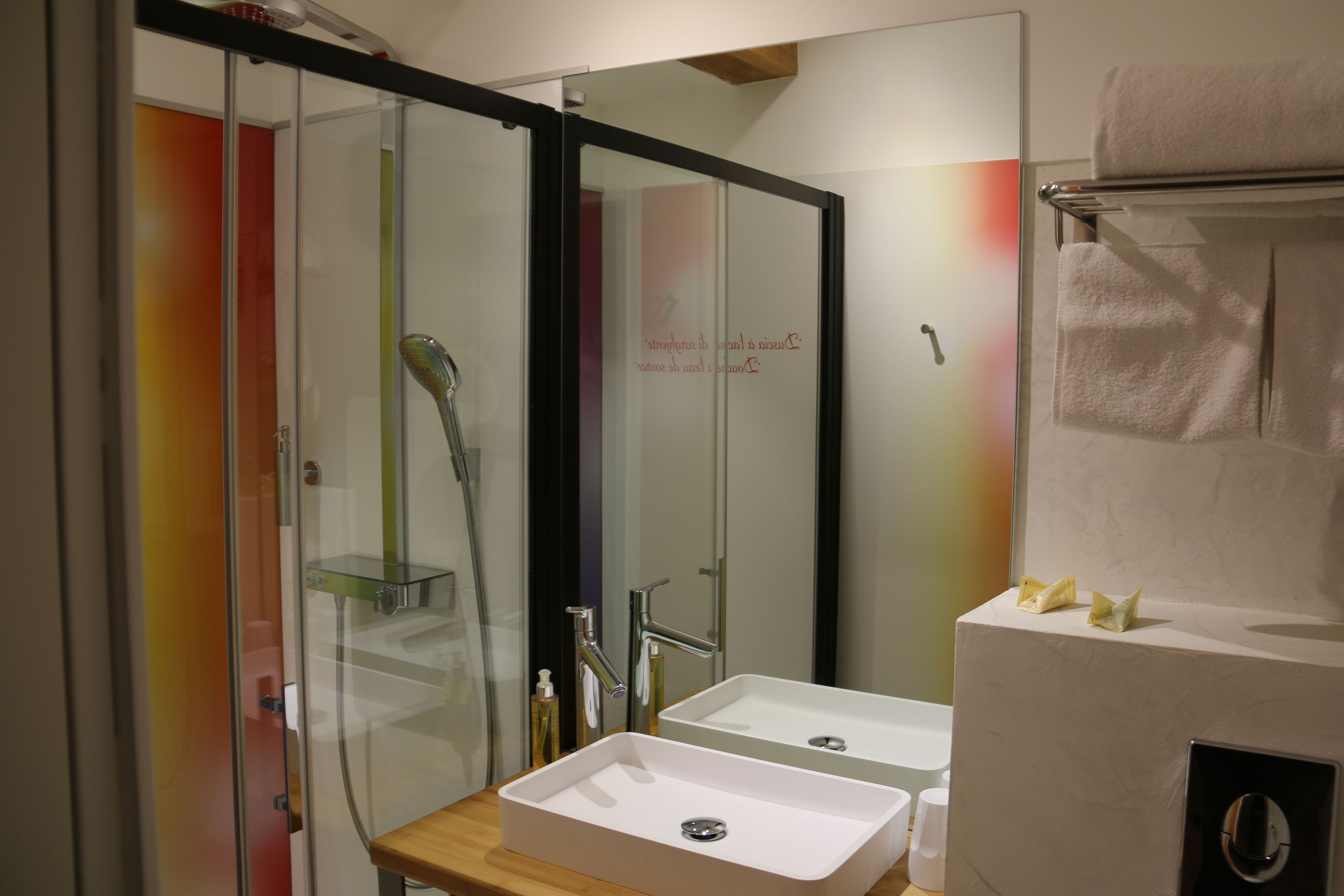 A modern bathroom with a glass shower enclosure, a white sink, and a towel rack.