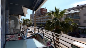 Un balcón de hotel con vistas a una calle, palmeras y un edificio con un cartel que dice 'HOTEL PANORAMA'.