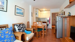 Una sala de estar con sofá, sillas, una mesa de comedor y una zona de cocina con armarios y un refrigerador.