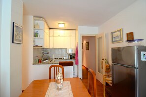 A compact kitchen with white cabinets, a stainless steel refrigerator, and a dining table with chairs.
