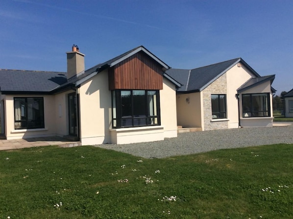 Une maison moderne à deux étages, dotée d’un grand porche à l’avant, d’une cheminée et d’une pelouse bien entretenue.